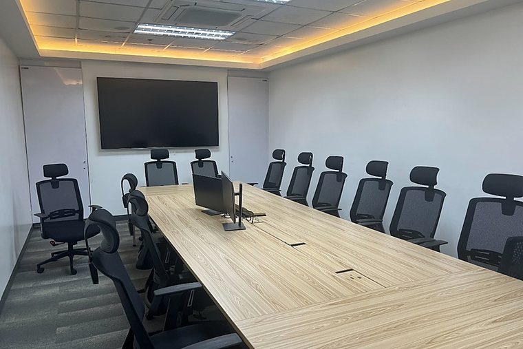 Meeting room with a long table, chairs and a large monitor.